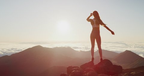 Young athletic woman standing on the edge of a cliff watching an epic sunrise, amazing outdoors fitness lifestyle