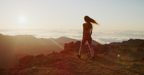 Young athletic woman walking to the edge of a cliff to watch the sun rise, epic outdoors fitness in slow motion