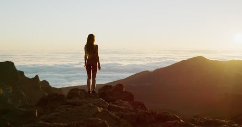 Young athletic woman raising her arms in success pose as she enjoys a breathtaking sunrise at the top of a mountain, sunrise fitness lifestyle in slow motion