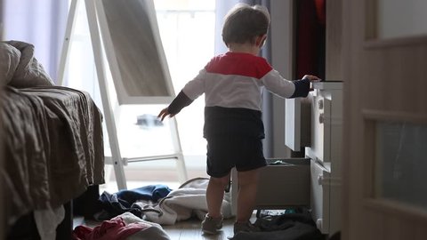 Little boy make a mess wit clothes in home. Candid view 