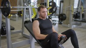 Sequence of two shots of muscular fitness blogger explaining and showing lying barbell bench press in gym while recording video lesson with professional camera