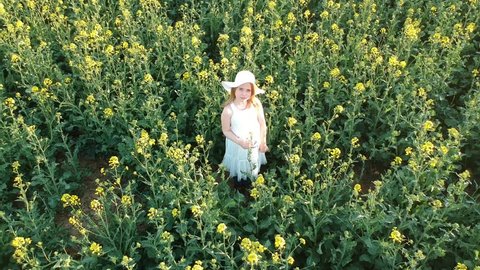 Aerial - Flying around little girl in white dress and hat in rape field