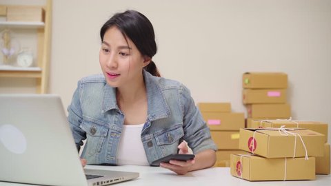 Smart Asian young entrepreneur business woman owner of SME online checking product on stock and save to laptop working at home. Small business owner at home office concept.