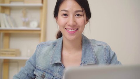 Asia business woman feeling happy smiling and looking to camera while relax at home office. Young asian woman working using laptop on desk in living room at home.