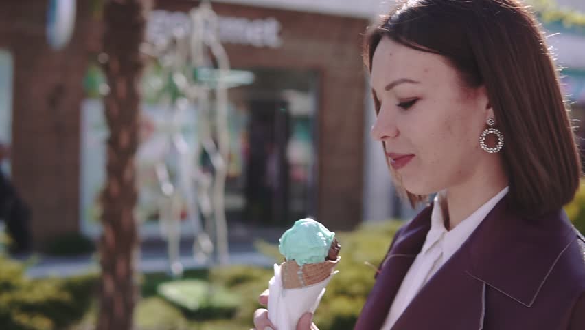 Adorable stylish brunette girl walking by broadwalk and eating ice-cream at sunny day