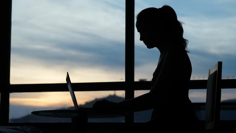 Woman finish work using laptop, close it and look to window, silhouetted shot. Sunset sky seen outdoors. Freelancer doing job concept
