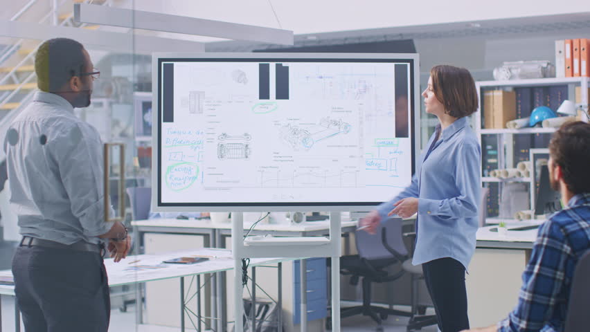 In the In Industrial Design Facility Team of Engineers and Technicians have a Meeting, Female Specialist Leads Briefing, Talks and Draws on Digital Interactive Whiteboard with Car Prototype Concepts Royalty-Free Stock Footage #1029099578