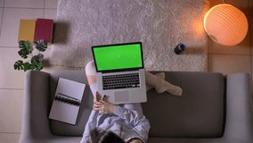 Closeup top shoot of young attractive female watching movie on the laptop with green chroma screen sitting on the couch in cute socks