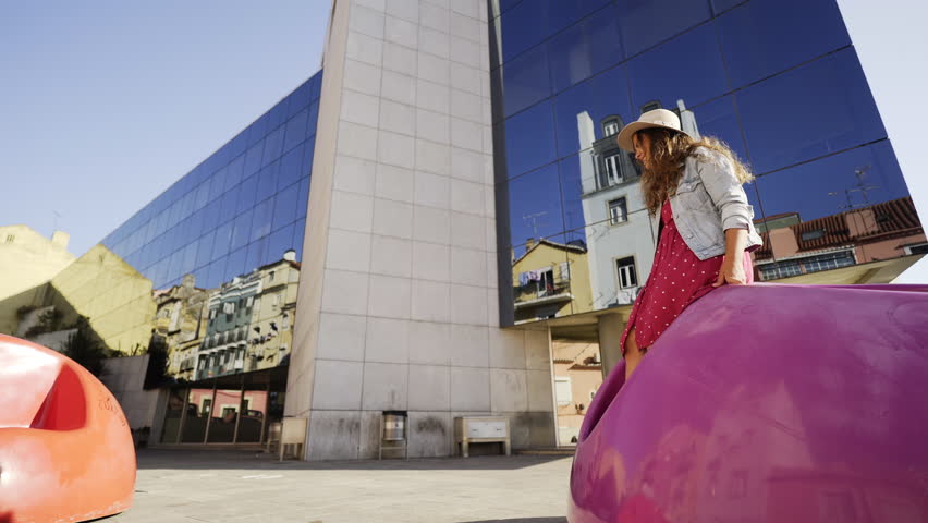 Side view man rolling on modern public chair to sitting woman and kissing at background office building with refflection city in glass wall