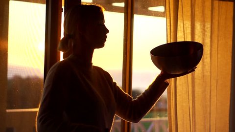 The girl on the background of the window at dawn engaged in Tibetan practice, performs massage sound vibrations with a tambourine and a bowl.