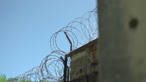 Prison or jail wall with razor wire against a blue sky. 