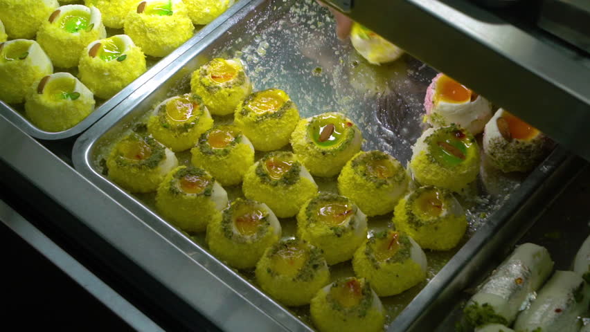A tray of sweet dessert on display at bakery.  The shop owner takes a treat off of the tray. Close Up. Handheld.