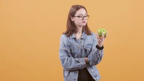 Teenage girl hold an apple in her hand and promotes healthy eating. Beautiful teen isolated over yellow background.