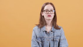Beautiful teenage girl in eyeglasses gets bored and yawns. Teenage girl covers her mouth while yawning over a yellow background.