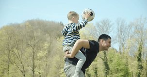 Father and son Soccer players in dynamic action funny play on the sand in football in grass, summer sunny day under sunlight. 4K slow motion video.