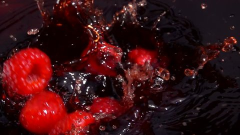 Ripe red raspberries fall into juice with beautiful splashes in slow motion
