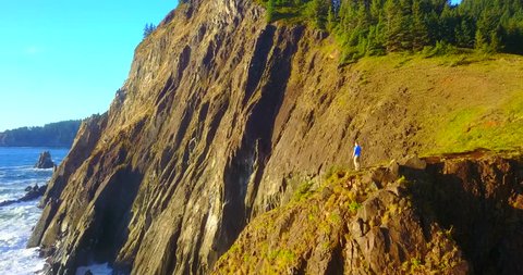 Lone Hiker Overlooking Sea From Rocky Cliffs In Treasure Cove, Oregon, USA - Aerial Zoom-Out