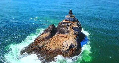 Rock Island With Lighthouse and Seals on Shore with Green Frothy Surf - Tillamook Rock, Oregon, USA - Aerial Overhead Zoom Out