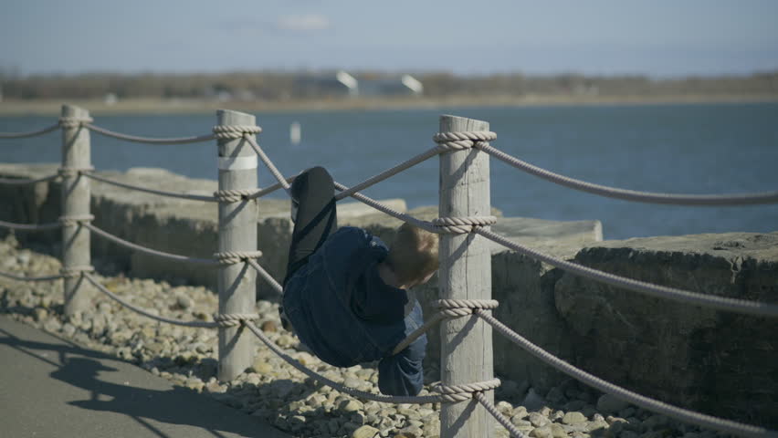Blond man tangled in a rope barrier next to a lake.
