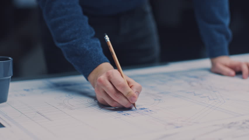 In the Dark Industrial Design Engineering Facility: Male Engineer Works with Blueprints Laying on a Table, Uses Pencil, Ruler and Digital Tablet. On Desktop Multiple Drawings. Focus on Hands Royalty-Free Stock Footage #1029171419