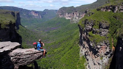 Man sitting on a rock at the edge of a cliff in front of the beautiful valley Vale do Pati, bahia - Brazil. With backpack after a trekking.
