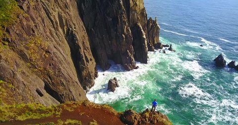 Isolated Hiker Looking Over Steep Seaside Cliffs at Treasure Cove, Oregon, USA - Slow Overhead Aerial Panning View