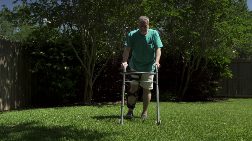 man using a walker and leg brace walks to camera showing scar on knee