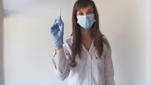 Young nurse in medical mask with stethoscope showing enema on white background