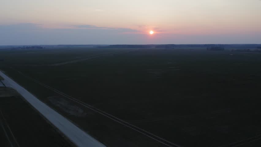 Aerial shot of a car driving on a dirt road, leaving dust behind, during a beautiful sunset