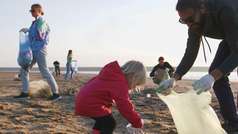 Little girl helps her parents to clean up area of dirty beach with garbage bags