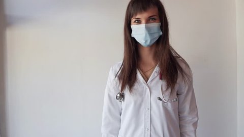 Young nurse in medical mask with stethoscope showing enema on white background