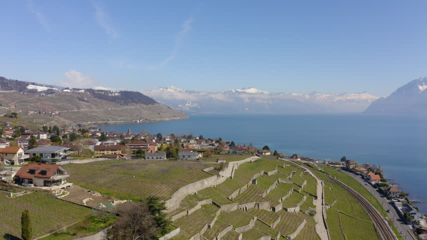 Aerial reveal over Grandvaux and Cully in Lavaux vineyard, spring season with snowy hills, Switzerland