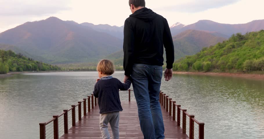 Parent and child go to the pontoon. Father and son walking on lake bridge