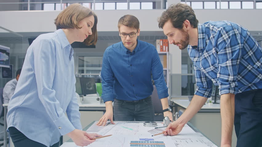 In the Industrial Engineering Facility: Female Designer Works with Industrial Engineer and Master Technician, They have Discussion, Analyse Engine Design Technical Drafts that are Lying on the Table Royalty-Free Stock Footage #1029209477