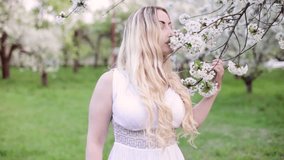 A young blond woman enjoys the scent of a blooming garden. The video becomes out of focus before finishing back in focus