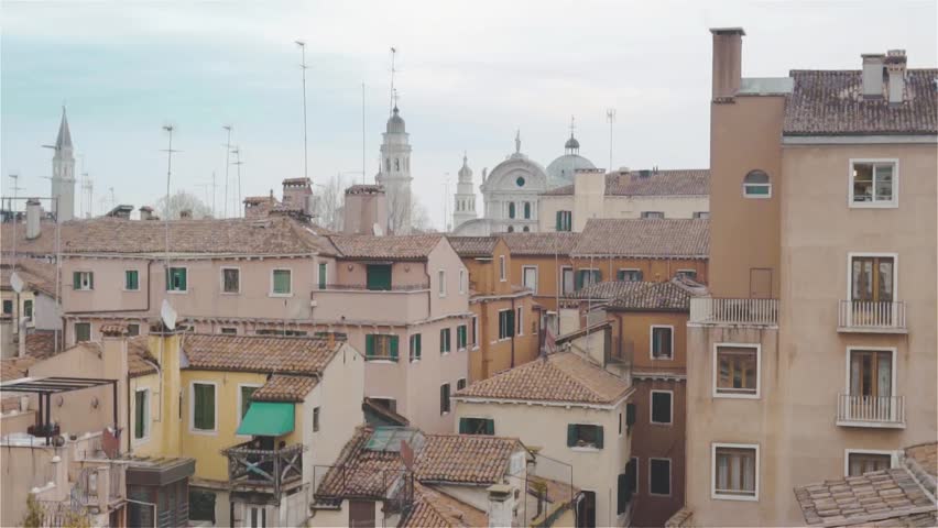 Tiled roofs of Venice. A lot of windows. Church on the blue clear sky. Spiers of towers and narrow streets. Aerial view.