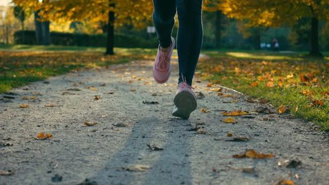 Runner Woman running walking in the fall park on sunny autumn day, close-up legs sport shoes,
