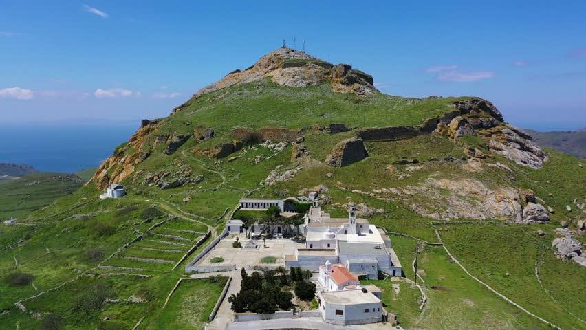 Aerial drone video of iconic Venetian Monastery of Sacred heart Pilgrimage at the bottom of mountain and castle of Exomvourgo or Exombourgo, Tinos island, Cyclades, Greece