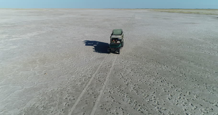 Aerial zoom out view of a 4x4 tourist safari vehicle driving on the wide open spaces of the Makgadikgadi Pans,Botswana