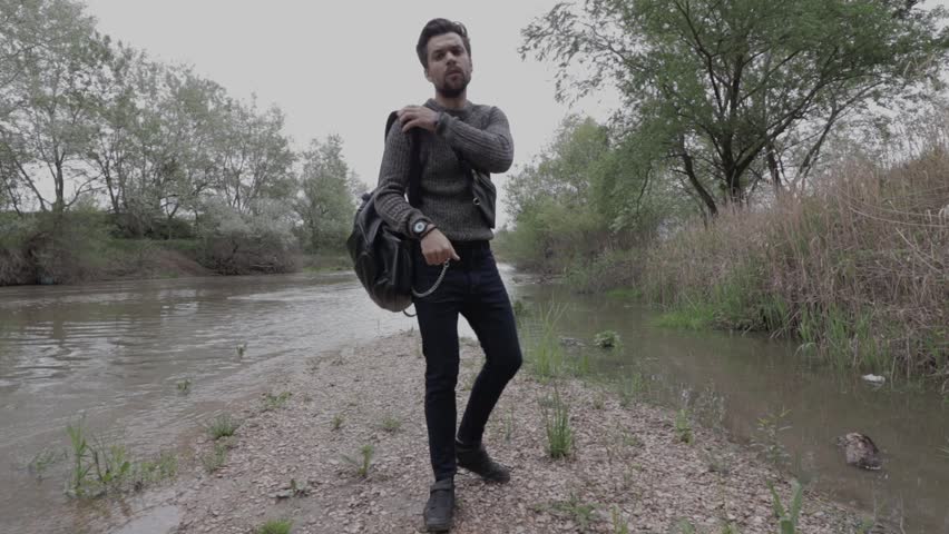 A man in nature, with a backpack walks through the woods along the river
