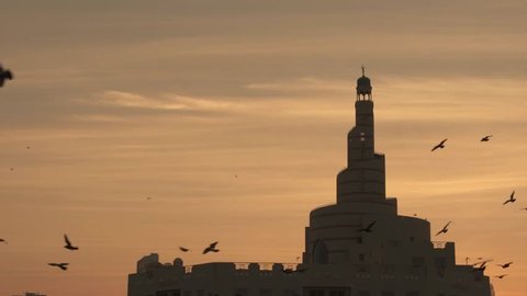 Early morning sunrise with birds flying and mosque in the background, Doha, Qatar.