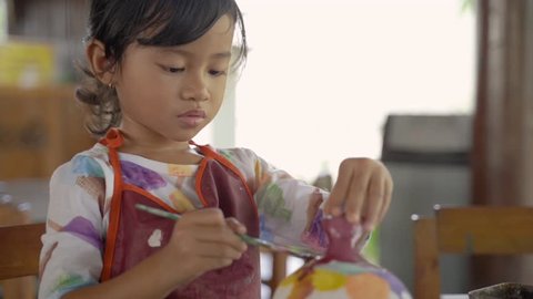 asian child painting ceramic pot with paint brush in pottery workshop