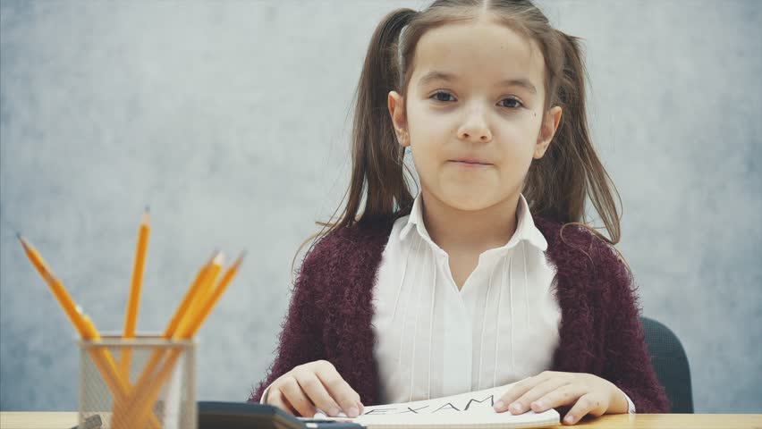 Young, hard-haired girl sitting at the table. During this inscription in the hands of the exam.
