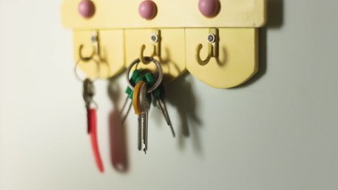 A male hand is hanging keys on a hook on the wall of a house. Selective focus