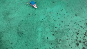 Aerial drone video of boat slowly moving through blue tropical waters.
