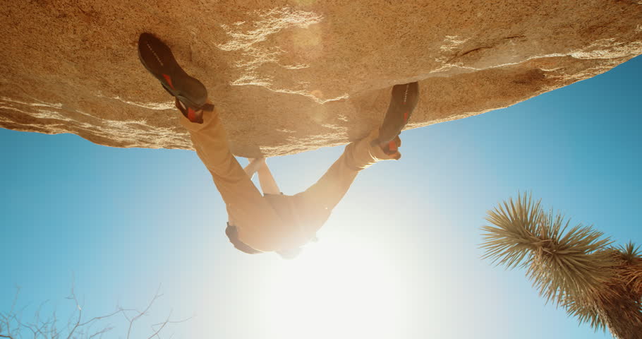 Low extreme angle of young man rock climbing reaching for hold with lens flare