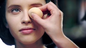 cropped view of makeup artist applying concealer under model eye with cosmetic sponge