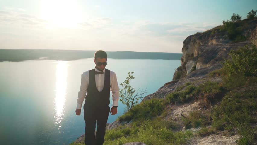 Couple walks out to ocean cliffs, takes in view together. Slow motion