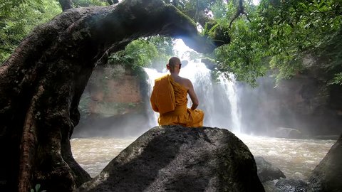 Buddhist monk in meditation at water fall on the mountain.