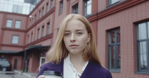 stylish beautiful woman with red hair in purple coat drinking coffee in paper cup in hand. Autumn and spring fashion trend, 4k video slow motion